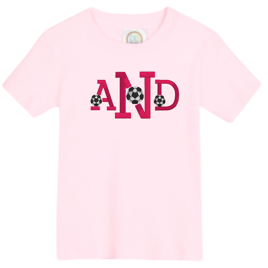 Pink t-shirt with 'AND' and soccer ball designs on a white background